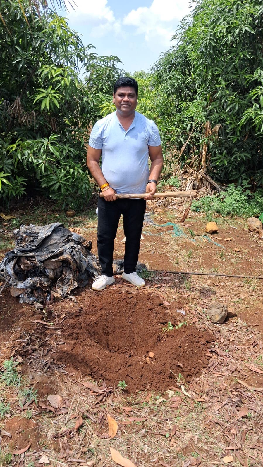 A volunteer stands beside a cleared pit of burnt waste on the land.